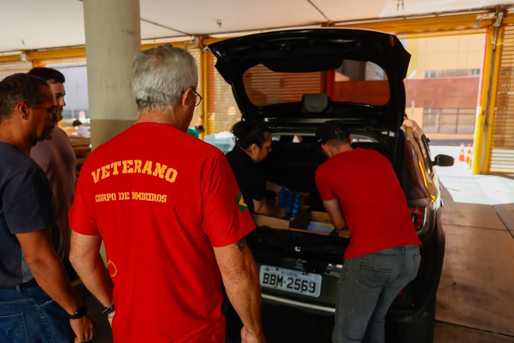 Corpo de Bombeiros recebendo doações, vestindo camisetas vermelhas e descarregando carro.