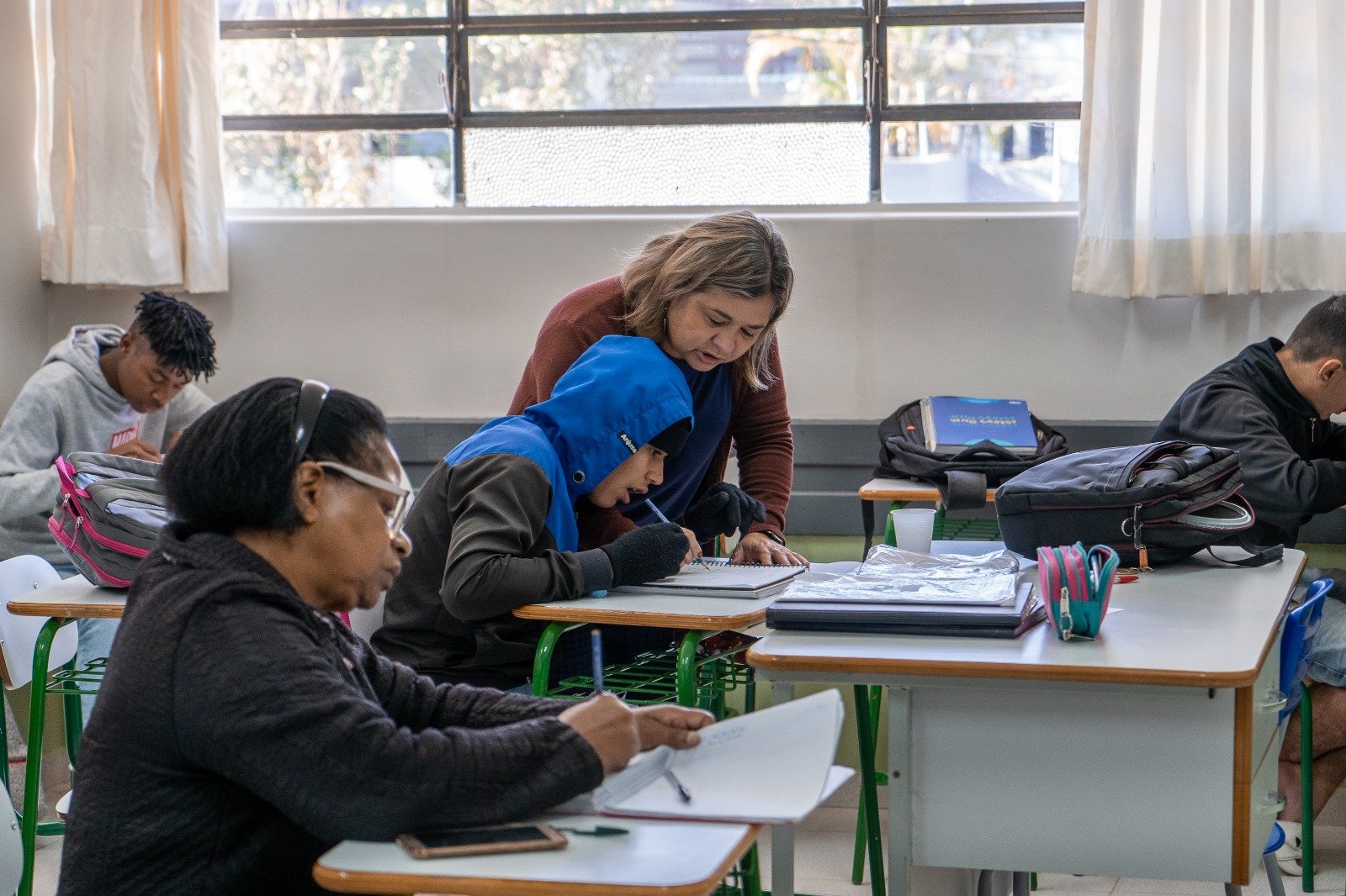 Imagem mostra uma sala de aula e um professor ensinando um aluno, mostrando que a taxa de alfabetização melhorou