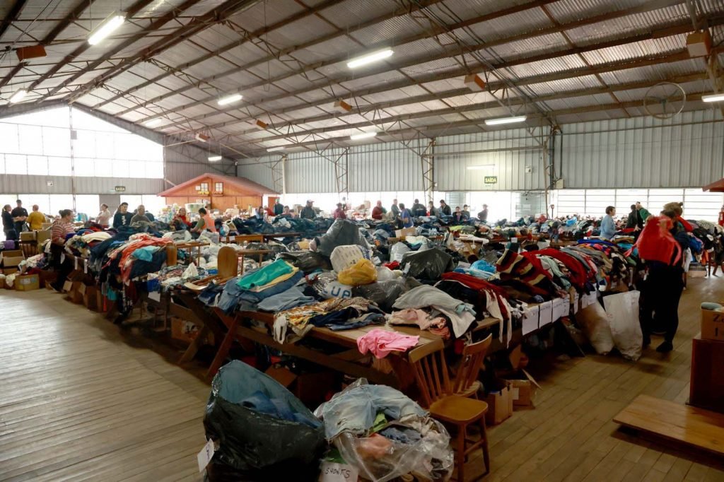 Diversas pilha de roupas que serão organizadas e distribuídas às vítimas no Rio Grande do Sul.