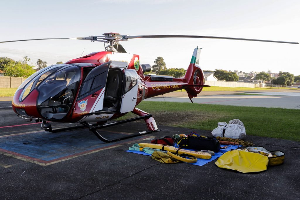 Helicóptero dos Bombeiros pousado com materiais que serão utilizados ao lado no chão, na missão do Rio Grande do Sul