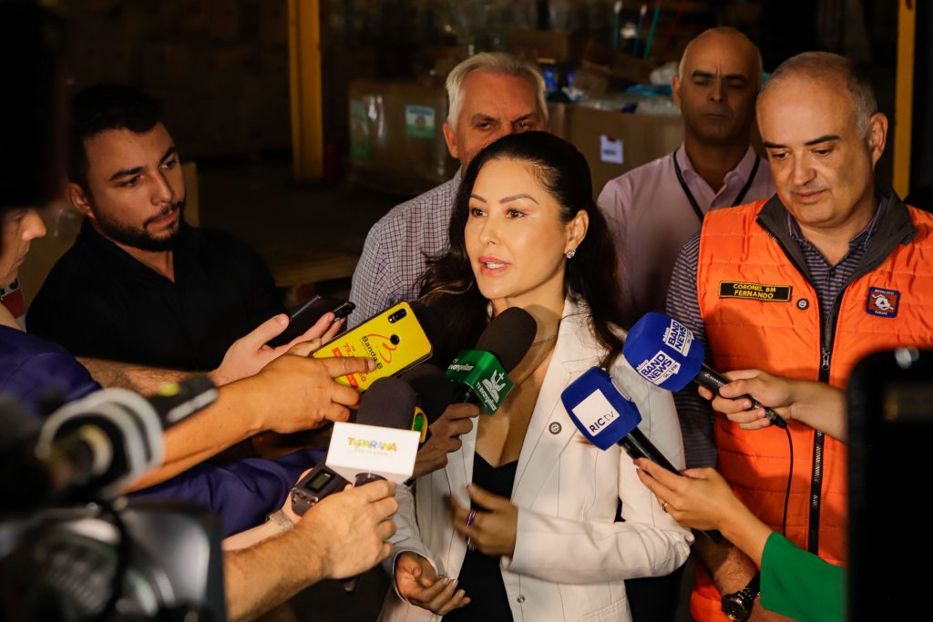 Primeira-Dama do Paraná concedendo a entrevistas para diversos veículos de comunicação. Está usando blusa preta e um casalo branco.