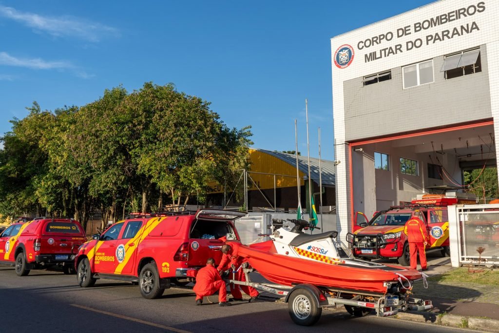 Três carros do corpo de bombeiros, um Jetsky e dois bombeiros encaixando o jetsky em um dos carros