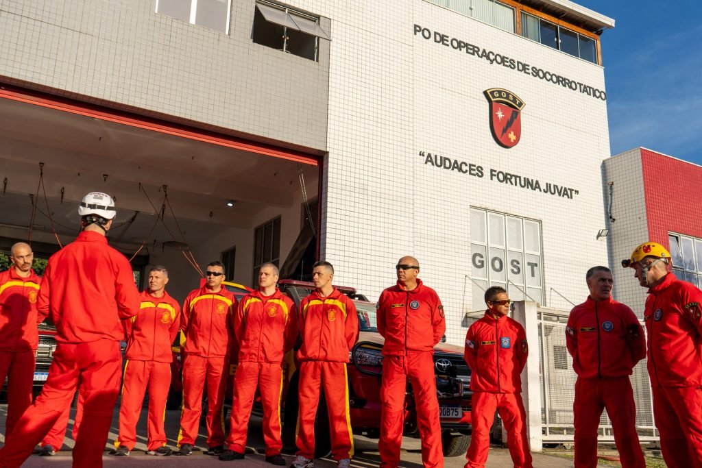 Vários bombeiros vestindo casacos e calças vermelhas.