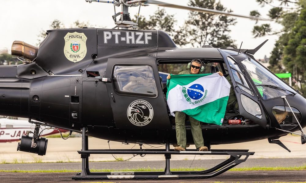 Helicóptero preto da PCPR com um homem segurando a bandeira do Paraná e sorrido