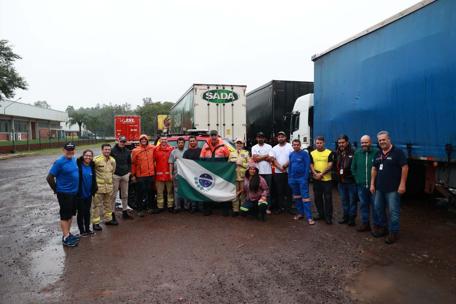 Imagem mostra diversas pessoas uma ao lado da outra, com a bandeira do Paraná na frente. São os voluntários que estão auxiliando na rede de ajuda humanitária