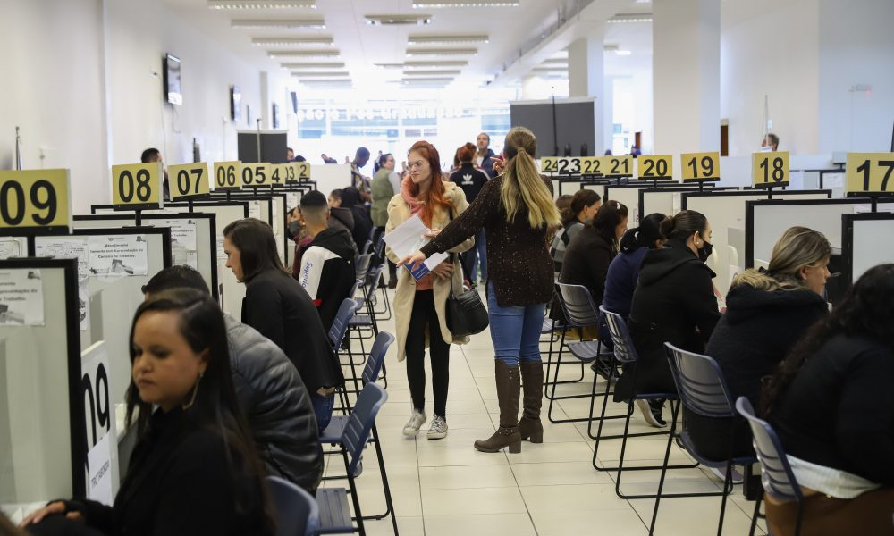 Imagem da sala de uma agência do trabalhador, com diversas pessoas sentadas em busca de bagas de emprego