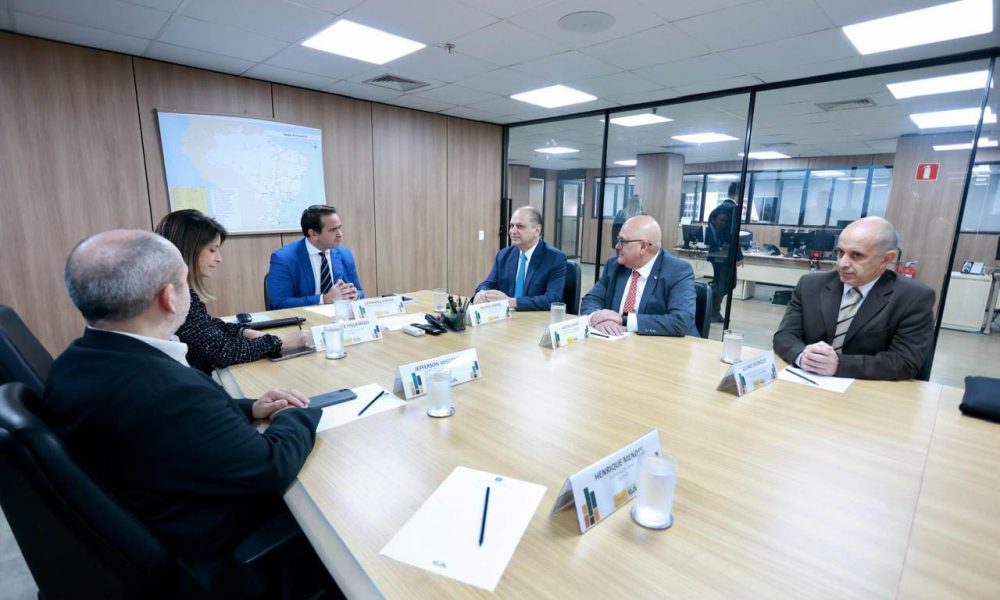 Imagem mostra uma sala de reunião com pessoas sentadas em uma mesa, conversando sobre a malha ferroriária do estado