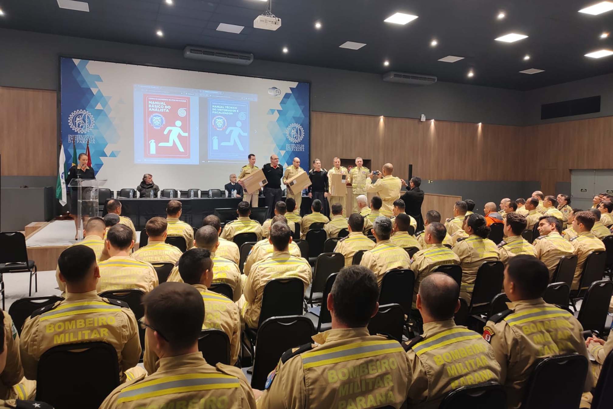 Imagem mostra a diversas pessoas em um auditório, participando da capacitação do corpo de bombeiros