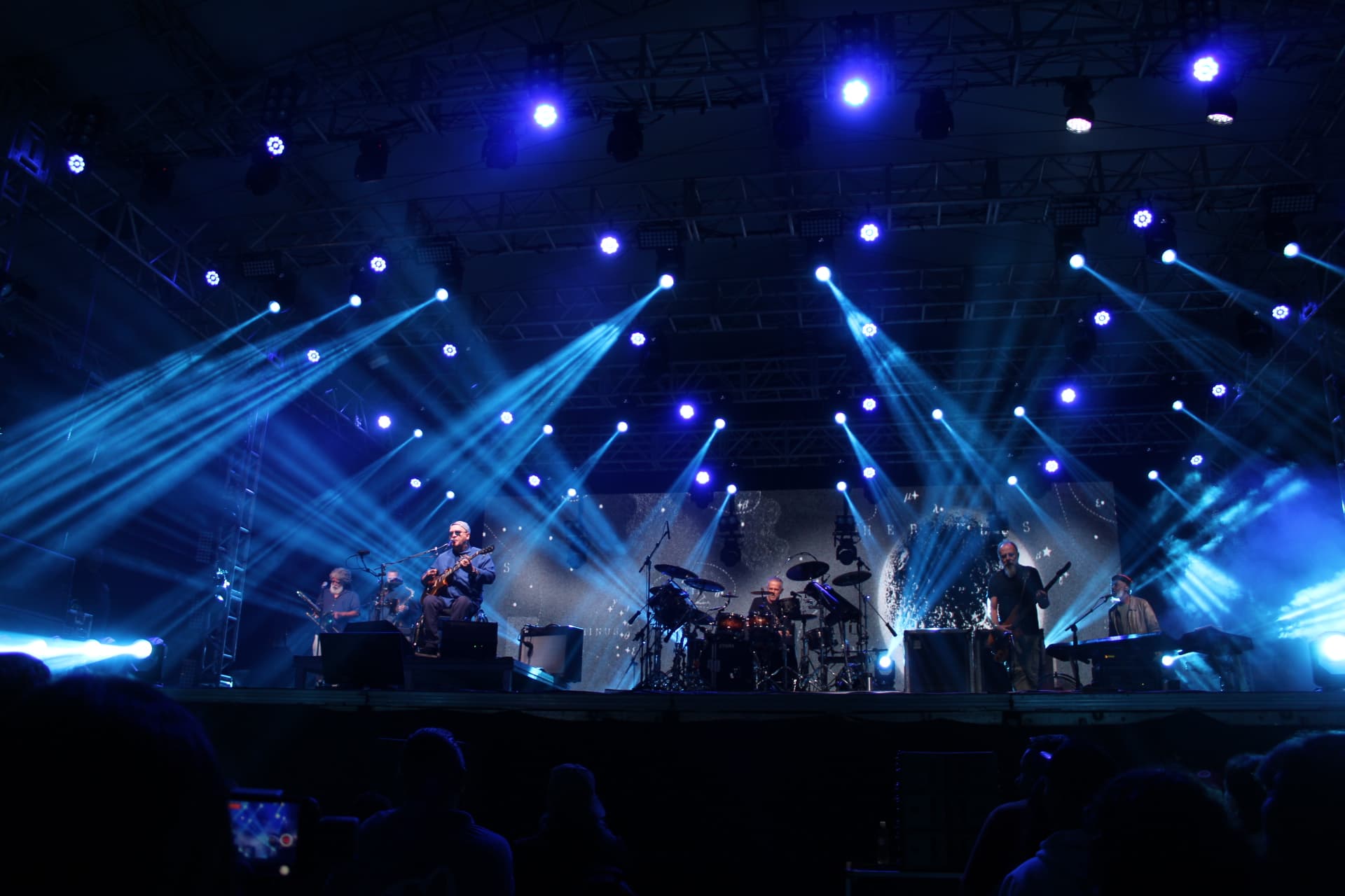 Imagem mostra a banda paralamas do sucesso em seu show em matinhos, a banda está em cima do palco, com diversas luzes no tom azul