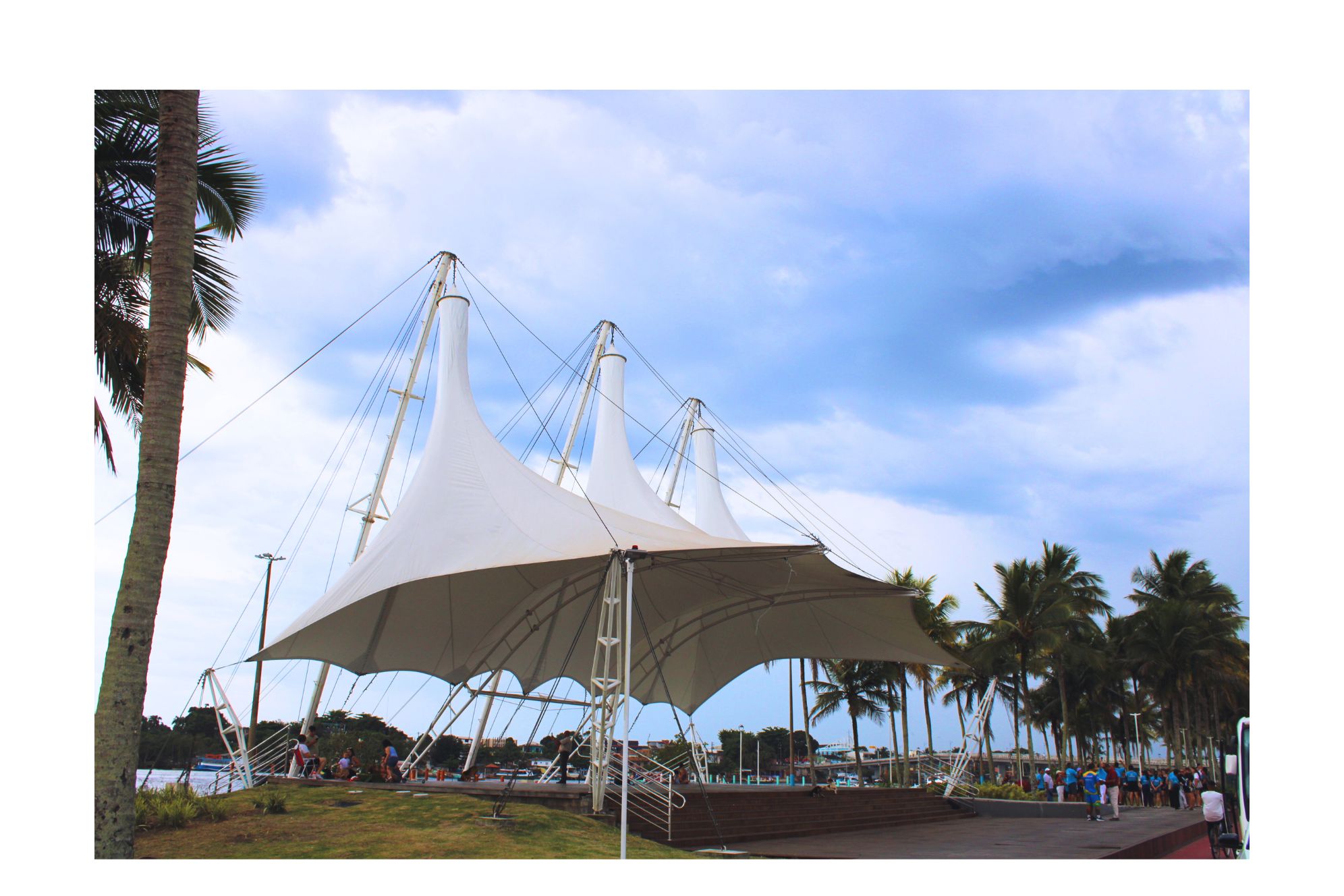 Estrutura de lona moderna em um ambiente ao ar livre, cercada por palmeiras e com céu azul ao fundo, ideal para eventos e lazer. Confira a programação para o fim de semana no Litoral do Paraná