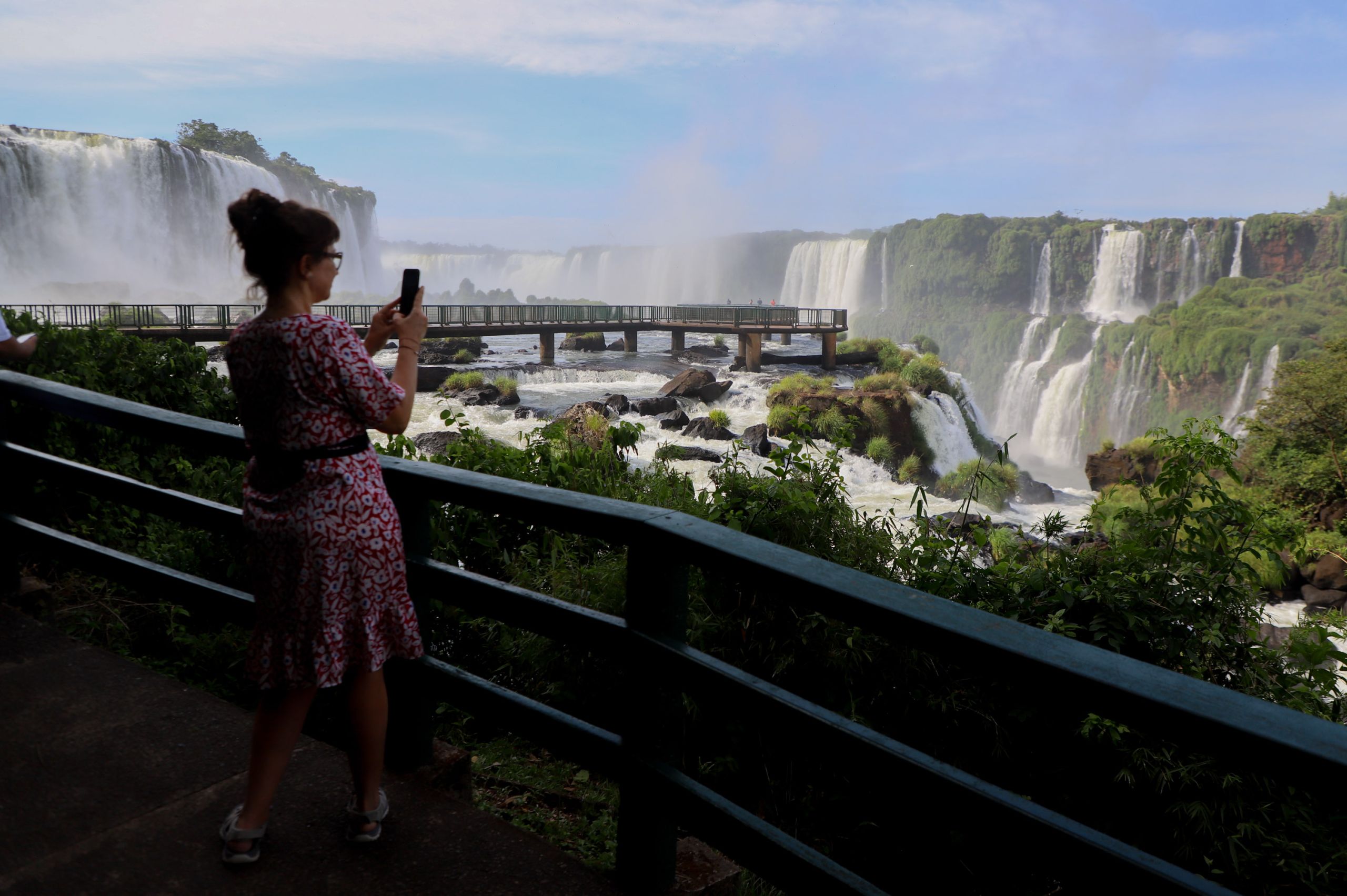 Mulher admirando as Cataratas do Iguaçu, registrando o belo cenário com seu smartphone. As águas impressionantes e a vegetação exuberante de fundo somam-se ao esplendor natural. O Paraná é o 3.º estado com maior número de turistas estrangeiros