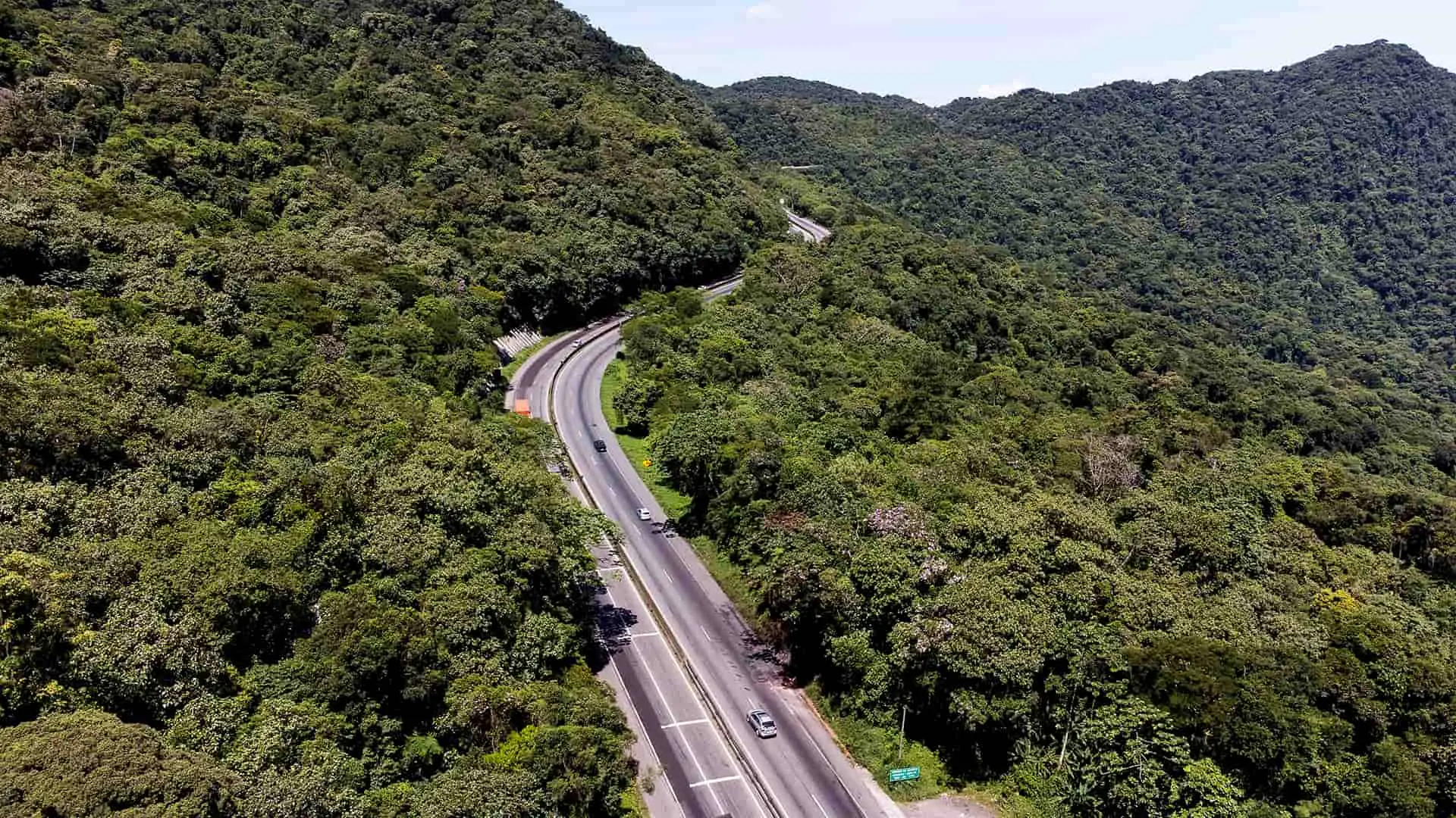 Vista aérea de uma estrada sinuosa cercada por uma densa vegetação verde. Esta imagem ilustra a beleza natural e a tranquilidade da br-277, viaduto dos padres, serra do mar no paraná