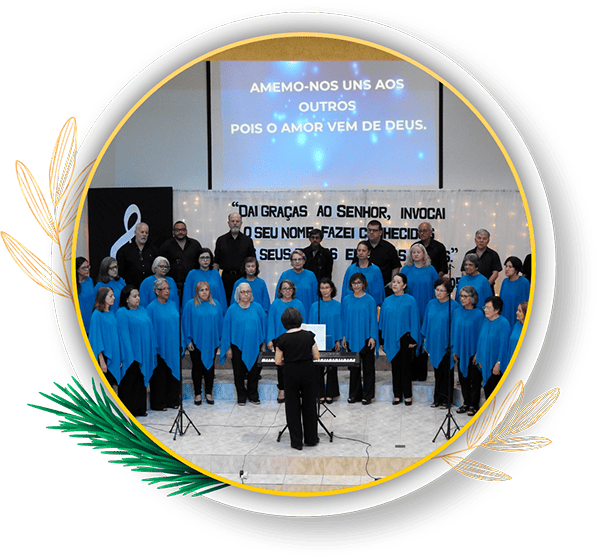 Coral se apresentando com vestimentas azuis, em um evento que destaca a mensagem de amor e união, com um telão ao fundo traduzindo a importância da amizade e comunhão. “Coro Hosanas”: há 94 anos levando a mensagem de Natal através da música. Grupo é conduzido pela maestrina Marília Cavallari na PIB de Paranaguá