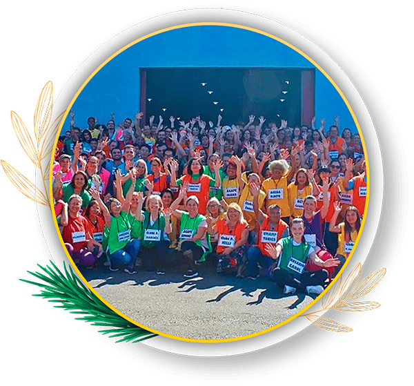 Grupo de pessoas felizes em um evento, todas levantando as mãos e vestindo camisetas coloridas, promovendo um ambiente de alegria e interação social. Feira da Partilha transforma sonhos em realidade em Paranaguá e no litoral do Paraná