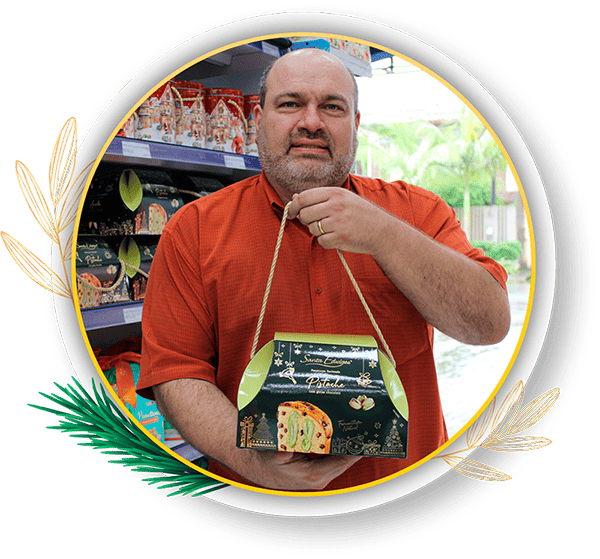 Homem segurando uma embalagem de panetone com pistache em uma loja.Ele está sorrindo e parece satisfeito com o produto que está apresentando.