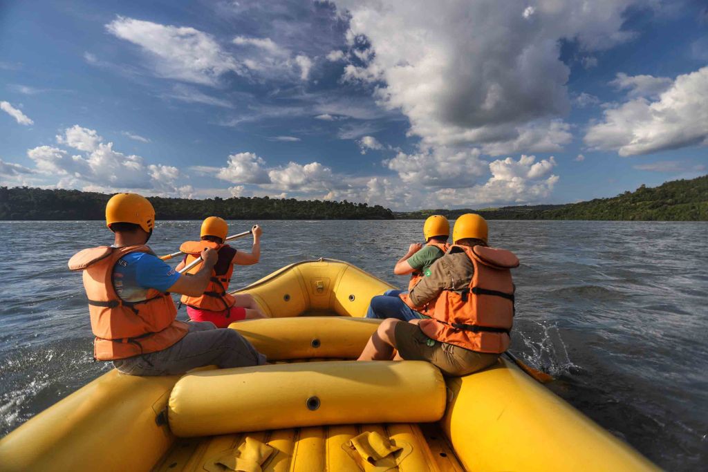 Excursão de rafting em um rio com quatro pessoas em um bote amarelo, usando coletes salva-vidas e capacetes, sob um céu azul com nuvens brancas. Turismo no Paraná cresce quase o triplo da média nacional entre janeiro e outubro