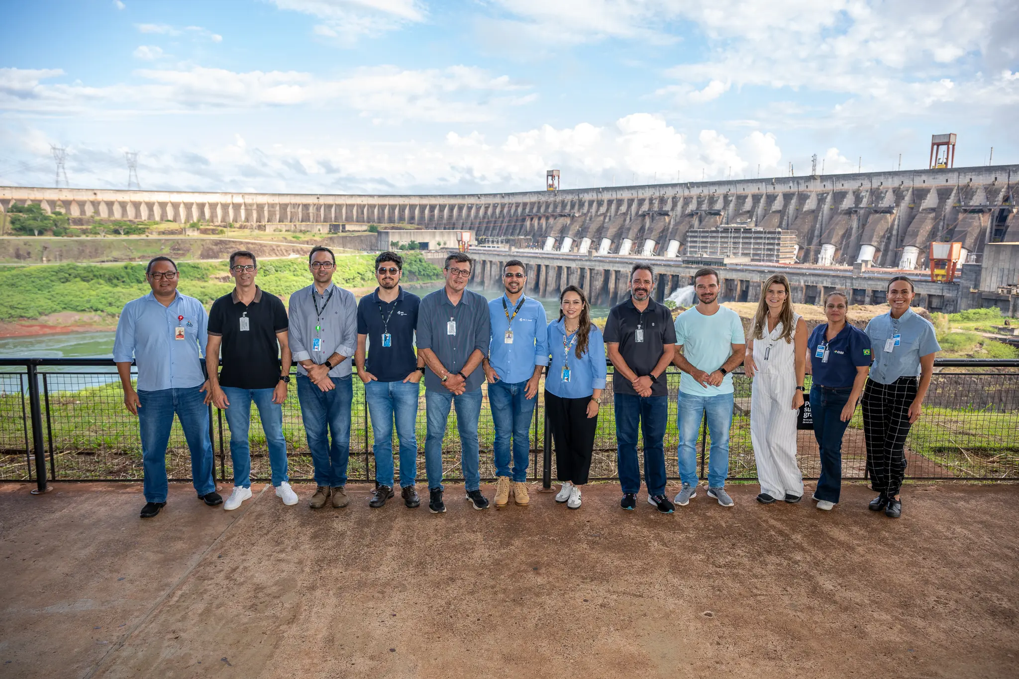 Grupo de profissionais posando em frente a uma grande represa, destacando a importância da engenharia e gestão de recursos hídricos.