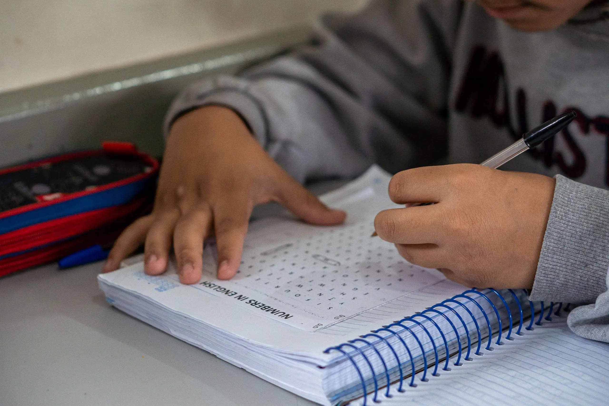 Criança escrevendo em um caderno enquanto resolve atividades escolares. A imagem destaca o envolvimento e o foco do estudante no aprendizado. Líder nacional em educação, Paraná vai receber aporte recorde de fundo federal