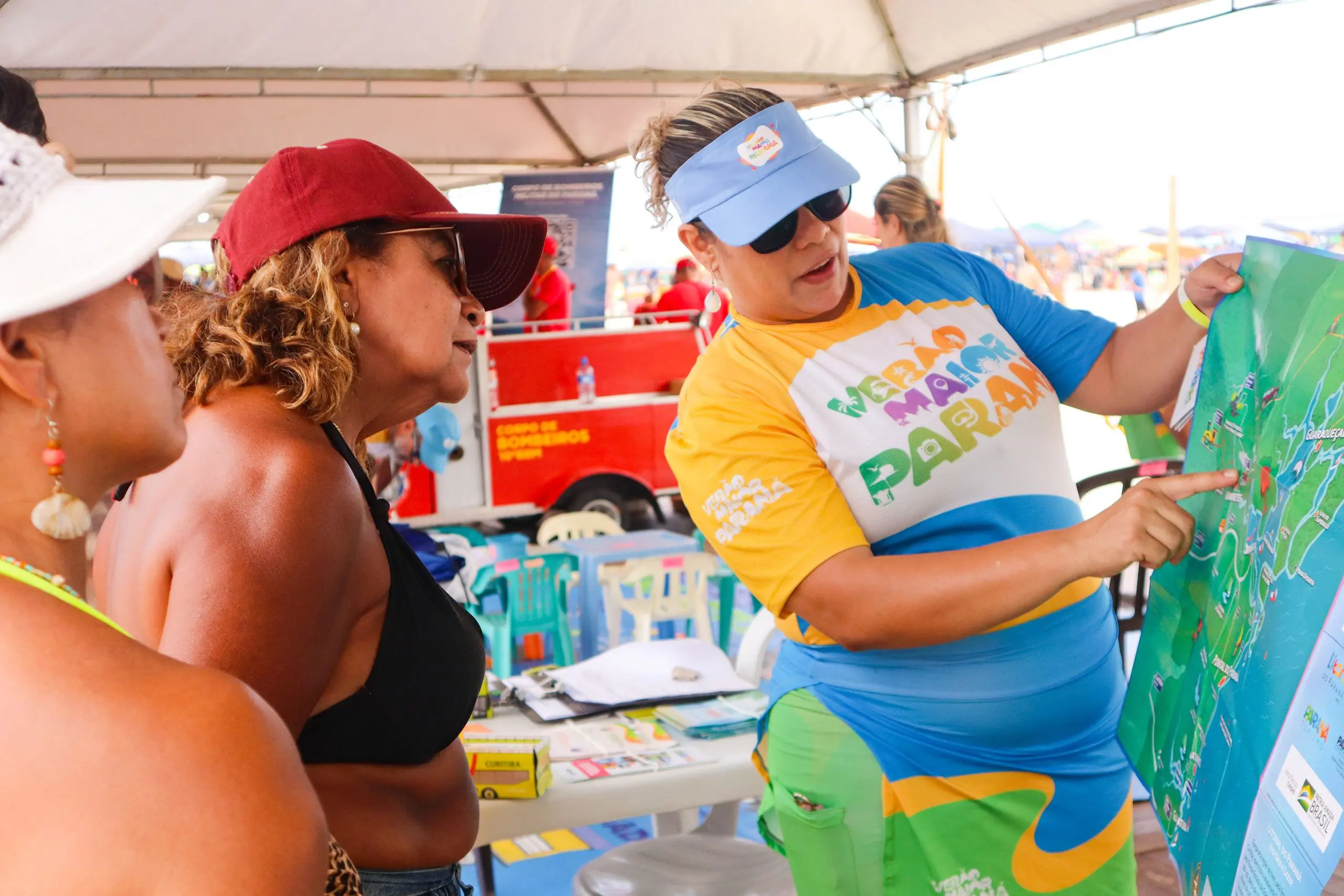 Mulheres em uma praia interagindo com uma apresentadora que mostra um mapa turístico, com diversas informações sobre a região. Mapas ilustrativos detalham atrativos do Litoral e do Noroeste