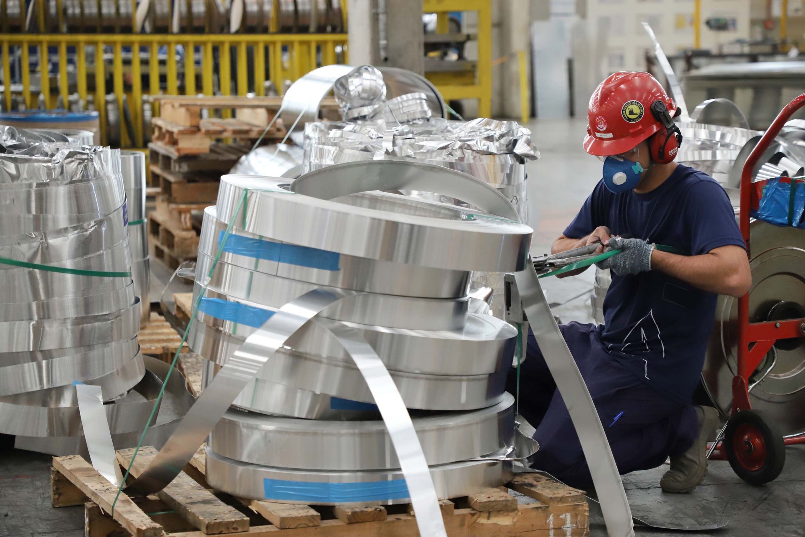 Trabalhador em fábrica manuseando bobinas de alumínio, utilizando ferramentas manuais para processamento. Ambiente industrial com foco em segurança e eficiência. Paraná se torna o 3.º maior empregador da indústria de transformação do Brasil