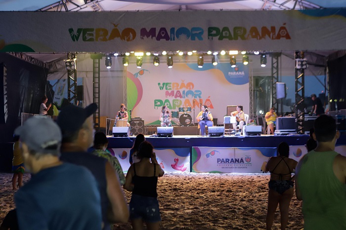 Evento Verão Maior Paraná com música ao vivo na praia, artistas se apresentando em palco iluminado, público animado. Cantora Brisan N’Tchalá e a Banda Coração Brasil sobem ao Palco Sunset neste sábado