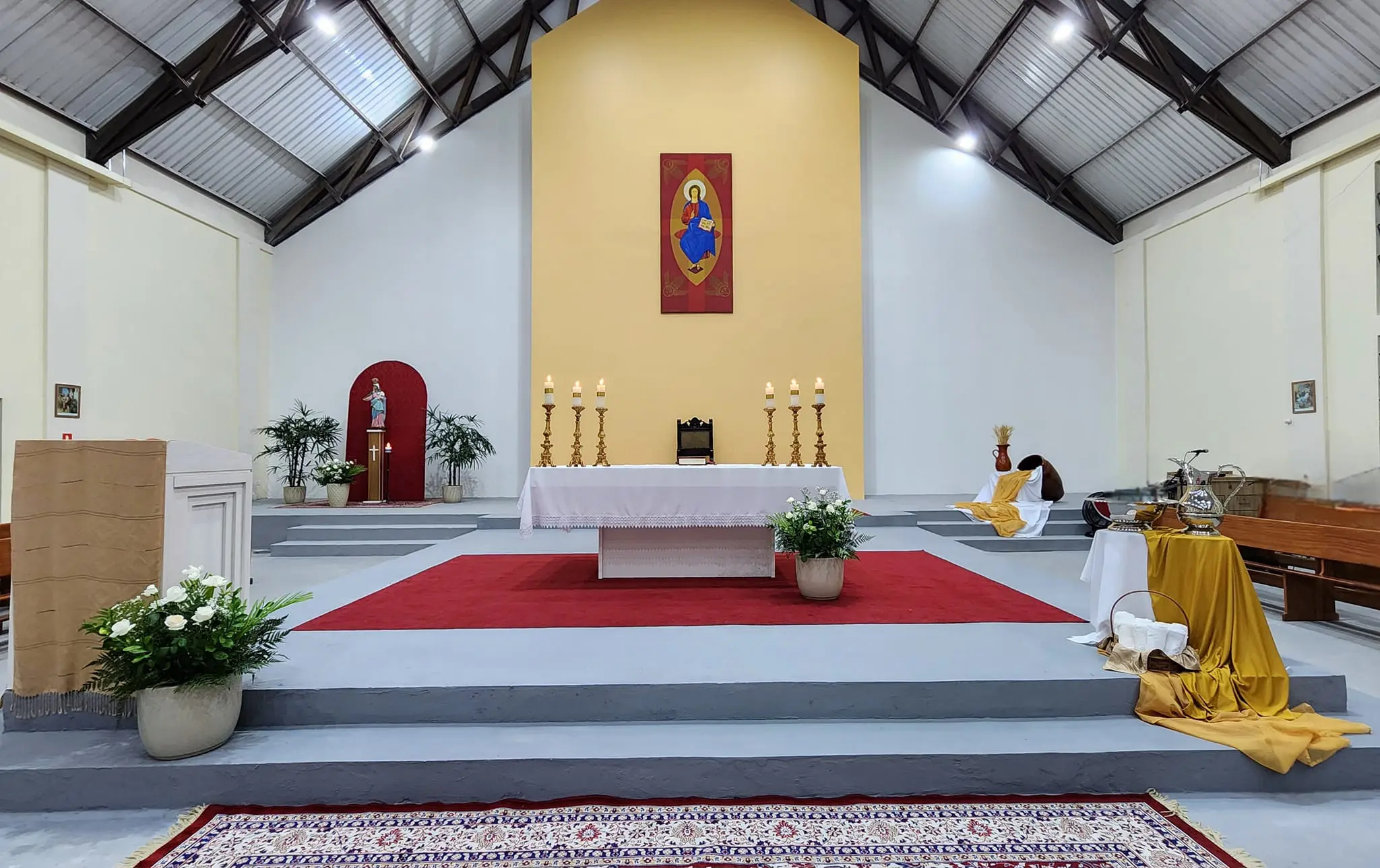 Imagem do altar de uma igreja com decoração simples, incluindo velas, flores e um tapete vermelho. Ambiente iluminado e acolhedor para celebrações religiosas. Missa em honra a São Francisco de Sales, patrono dos jornalistas e escritores, acontece em Paranaguá