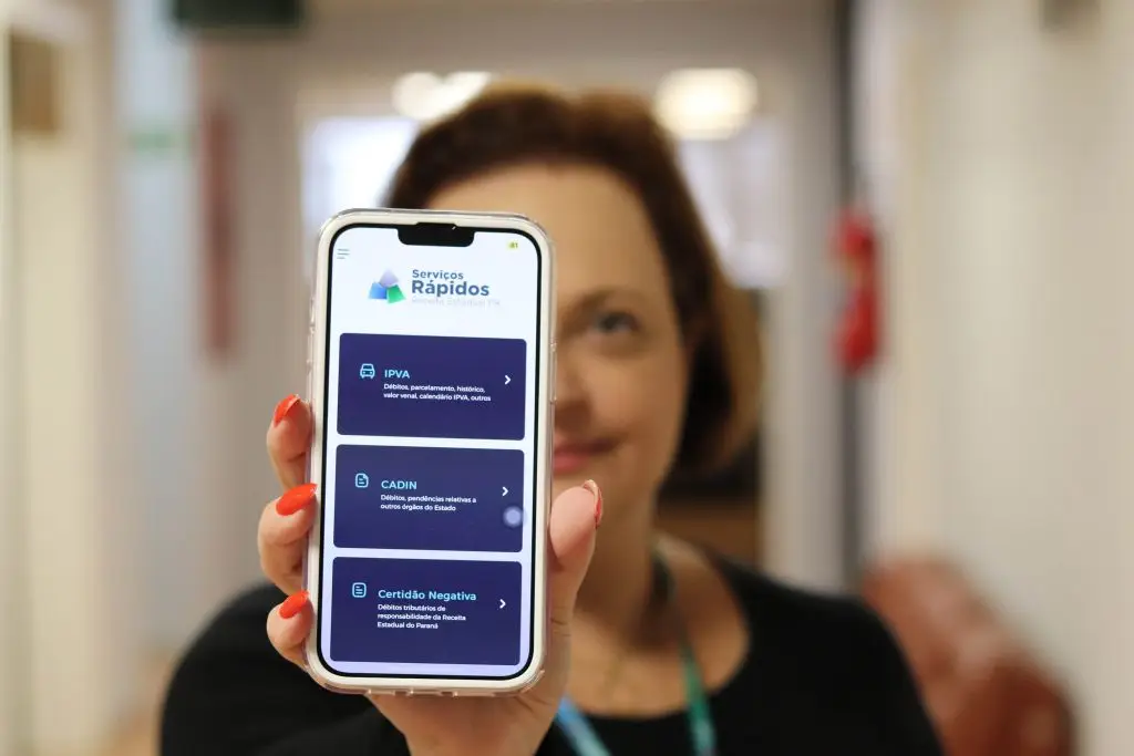 Imagem de uma mulher segurando um smartphone mostrando os serviços rápidos do IPVA, CADIN e Certidão Negativa, destacando acesso fácil a informações importantes. Cota única e primeira parcela do IPVA vence na próxima semana; veja como pagar
