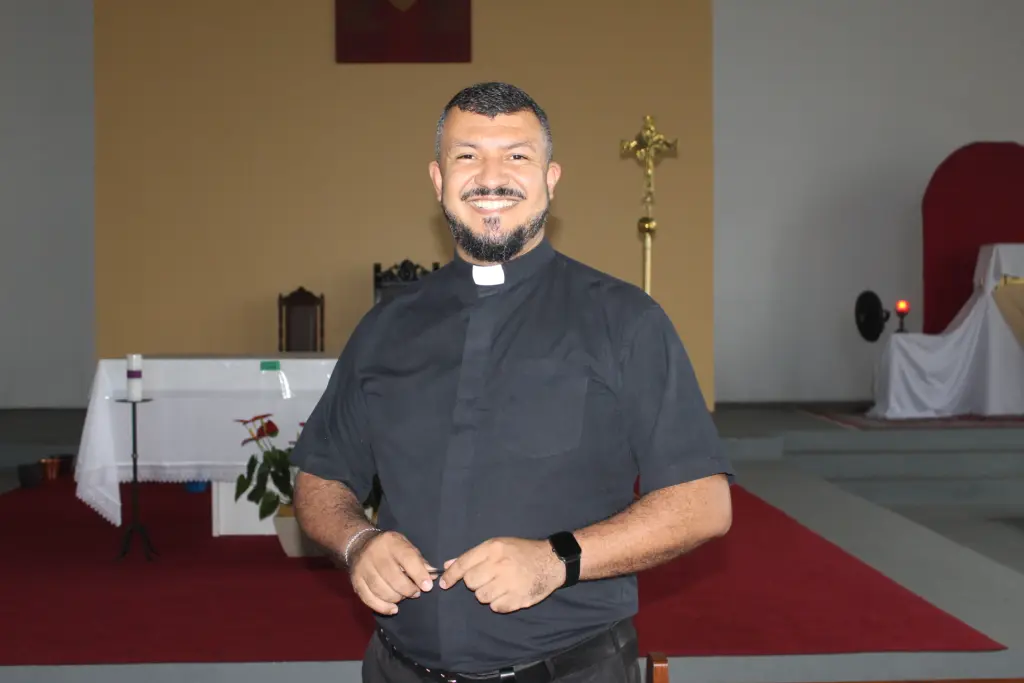 Imagem de um padre sorridente em uma igreja, com vestimenta clerical, em ambiente iluminado e acolhedor, transmitindo alegria e paz espiritual. Missa em honra a São Francisco de Sales, patrono dos jornalistas e escritores, acontece em Paranaguá