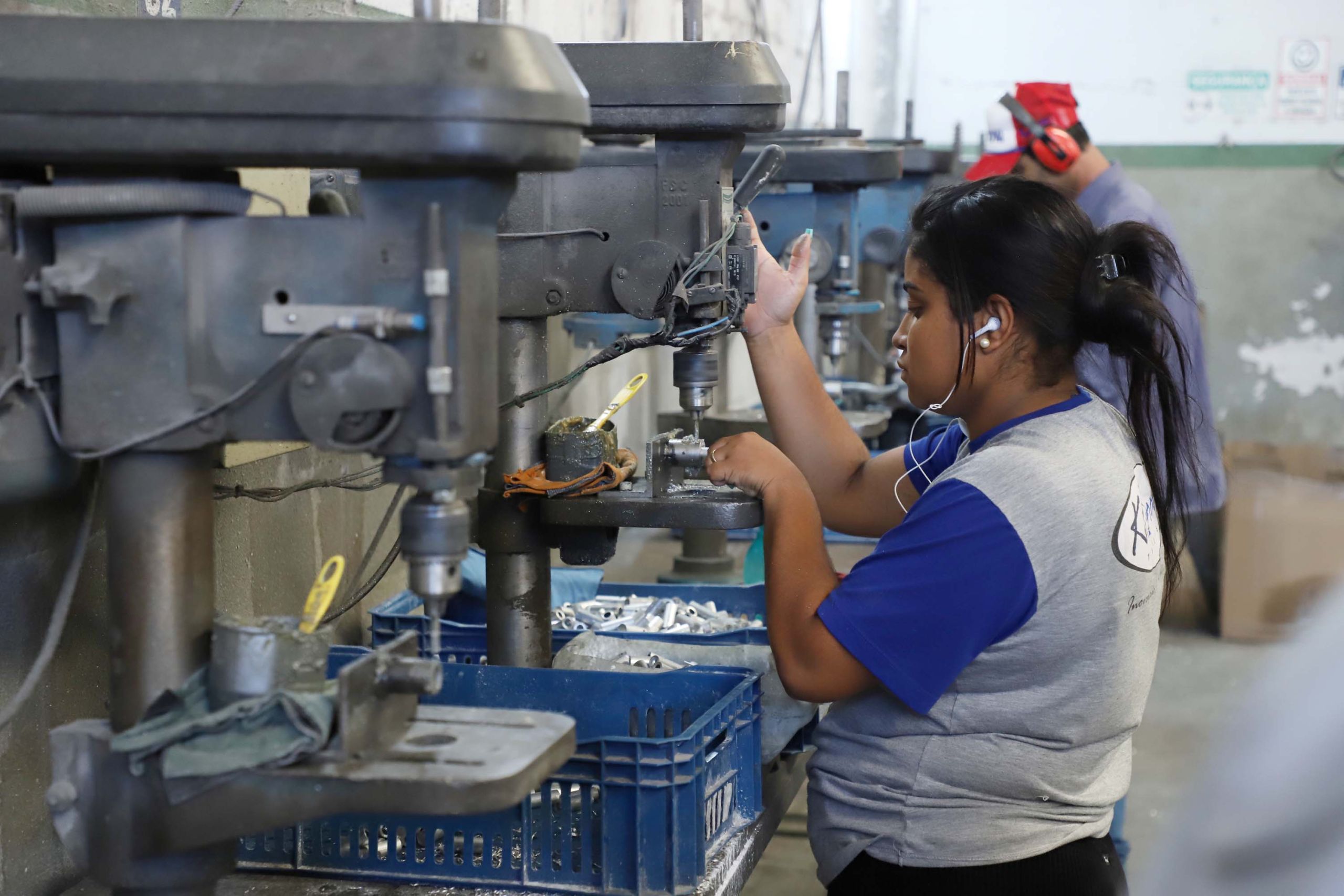 Imagem mostrando uma mulher trabalhando em uma máquina perfuradora em um ambiente industrial, evidenciando a importância do trabalho feminino na indústria. Com indústria no topo, Agências do Trabalhador reúnem 22,5 mil vagas de emprego