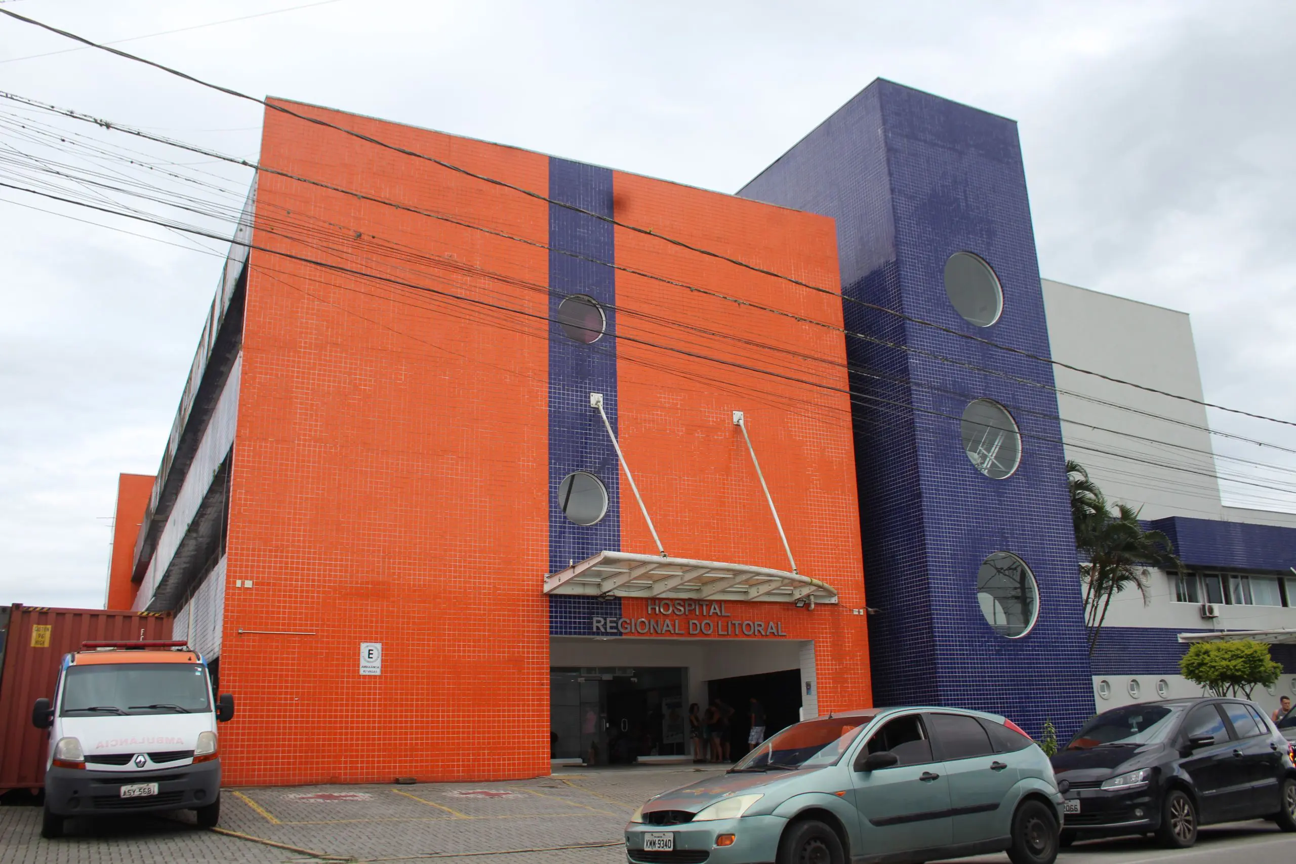 Imagem do Hospital Regional do Litoral, com fachada colorida em tons de laranja e roxo, destaque para a entrada e veículos estacionados. Governo investe R$ 5,1 milhões para reforçar atendimento no Hospital Regional do Litoral