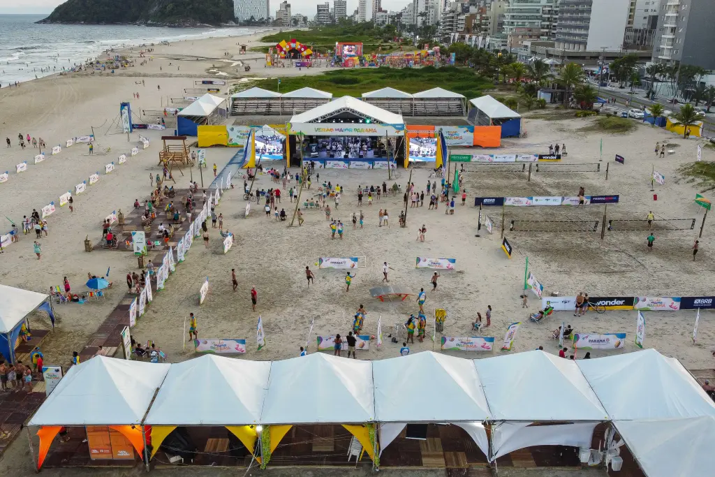 Vista aérea de um evento na praia, com palcos e tendas, onde pessoas participam de atividades recreativas e esportivas Nova infraestrutura das praias paranaenses impressiona turistas estrangeiros
