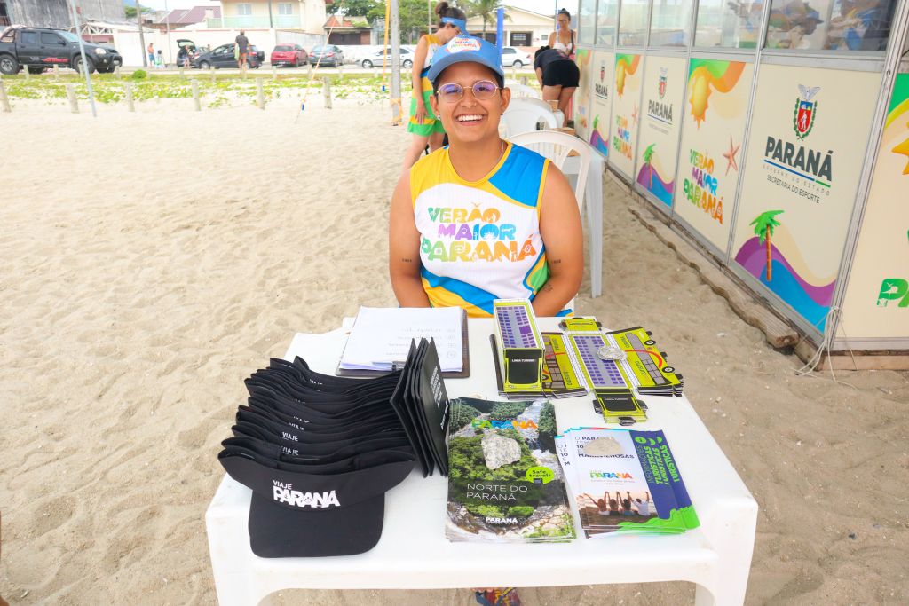 Uma pessoa sorridente em uma tenda de verão no Paraná, cercada por materiais promocionais e acessórios do estado, com uma atmosfera alegre de praia. Mapas ilustrativos detalham atrativos do Litoral e do Noroeste
