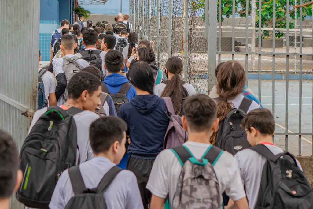 Grupo de estudantes caminhando com mochilas em direção a uma escola, representando a rotina escolar e a vida acadêmica.