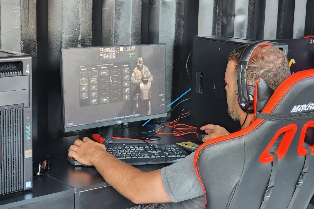 Jogador focado em um jogo de tiro no computador, utilizando um headset e sentado em uma cadeira gamer vermelha e preta. Final de torneio de eSports vai agitar Caiobá no domingo no Verão Maior Paraná