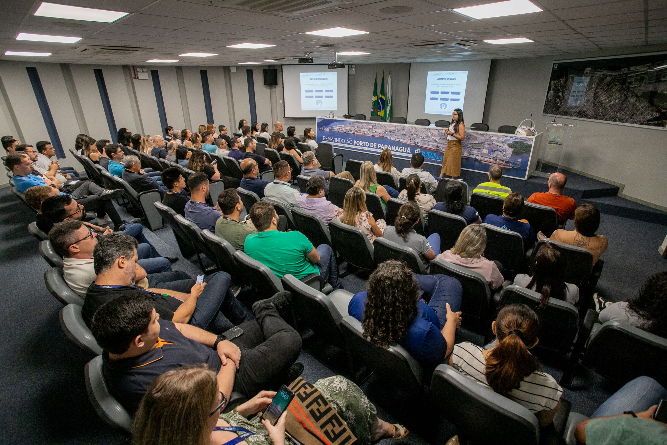 Auditorio cheio durante apresentação no evento sobre o Porto de Papaquagá, com palestrante e participantes atentos em um ambiente moderno. Portos do Paraná realiza evento interativo sobre saúde mental e emocional