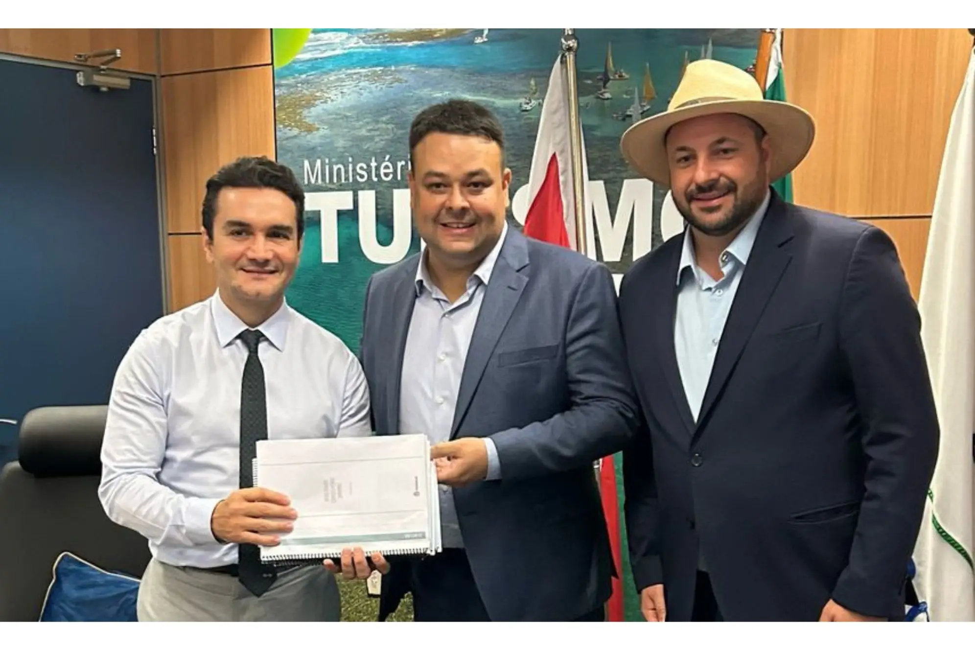 Foto de três homens em reunião no Ministério do Turismo, segurando documentos importantes para o setor turístico no Brasil. Secretário de Governo busca recursos para Paranaguá em Brasília