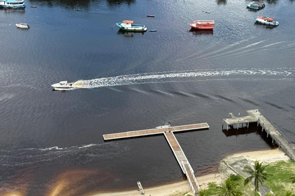 Vista aérea de um rio com barcos, um píer e vegetação ao redor, ideal para relaxamento e lazer. A imagem captura a tranquilidade do cenário aquático. Com investimento de R$ 6,7 milhões, IAT começa a instalar novos flutuantes no litoral