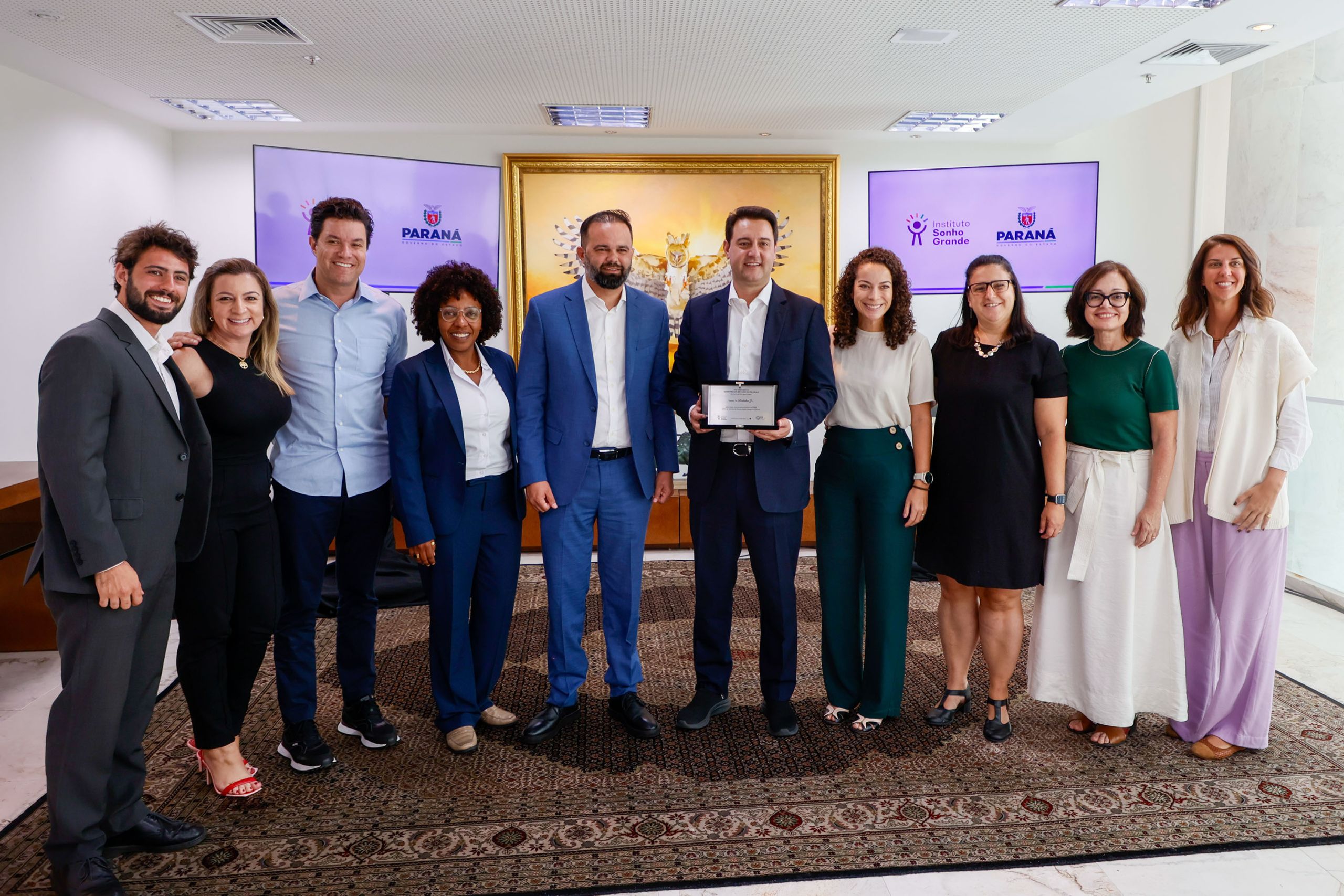 Grupo de pessoas posando em evento oficial no Paraná com certificado de reconhecimento. A cerimônia destaca a importância do trabalho em equipe e inclusão. Líder no Ideb, Paraná reforça parceria com institutos para avançar na educação