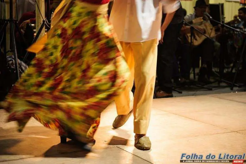 Um casal dança animadamente em uma apresentação cultural, destacando seu vestuário colorido e o ritmo da música tradicional. Baile do Fandango Caiçara acontece neste sábado, na Associação Mandicuera