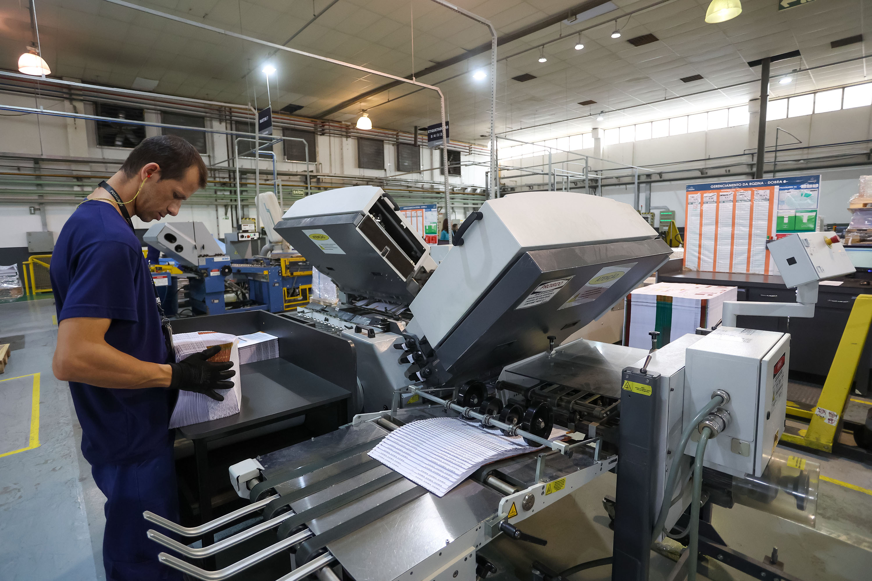 Funcionário operando uma máquina de impressão em uma gráfica, com destaque para a produção de impressos. O ambiente é bem iluminado e organizado. Paraná abre 15,9 mil vagas de emprego em janeiro e chega a 124 mil nos últimos 12 meses