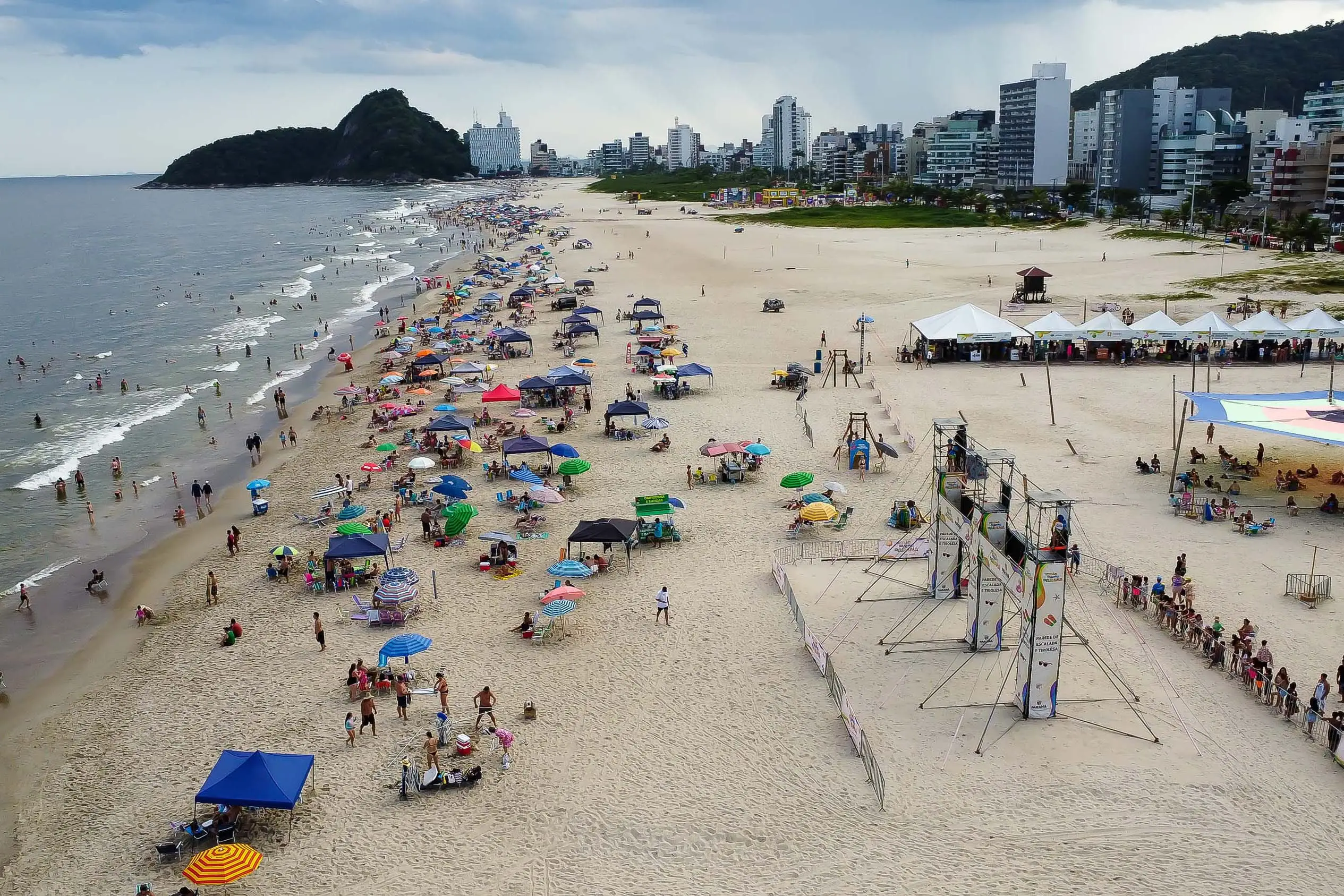 Vista panorâmica da praia movimentada com muitas pessoas e guarda-sóis, ideal para lazer e turismo, mostrando a beleza do litoral. Programação e atividades do Verão Maior têm 85% de aprovação entre paranaenses