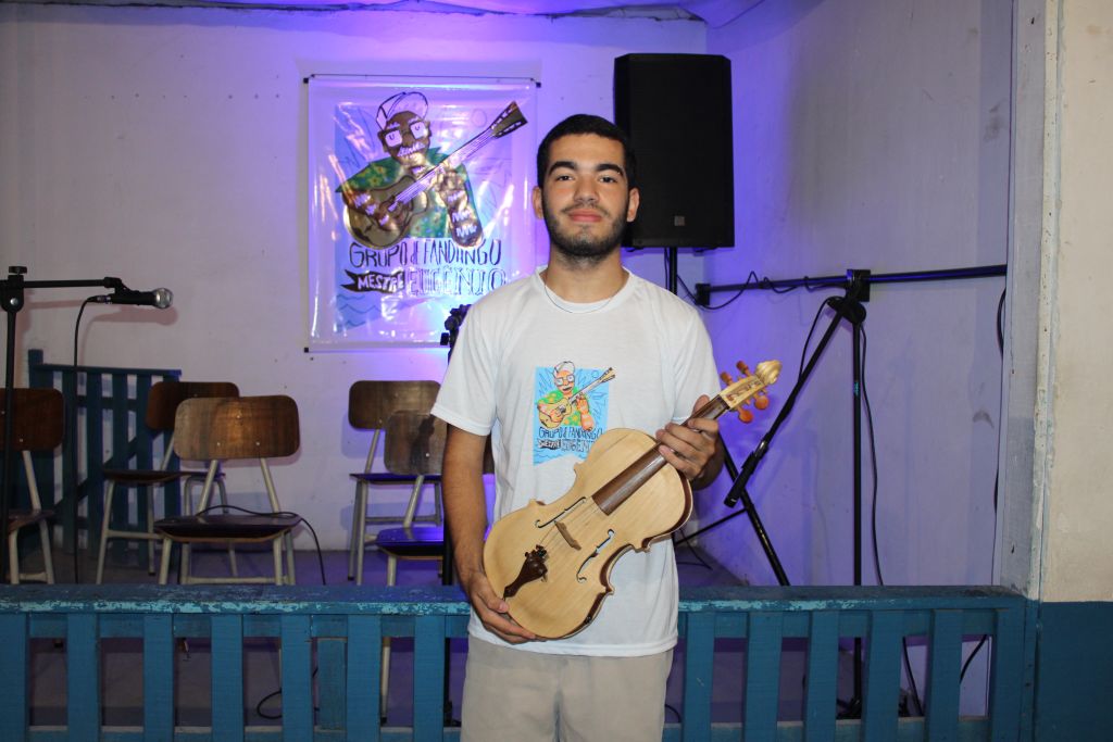 Jovem segurando um instrumento musical, posando para a foto em um ambiente festivo, evidenciando a cultura musical do Grupo Plandeando. Baile de Fandango Caiçara acontece dia 15 de fevereiro em Paranaguá
