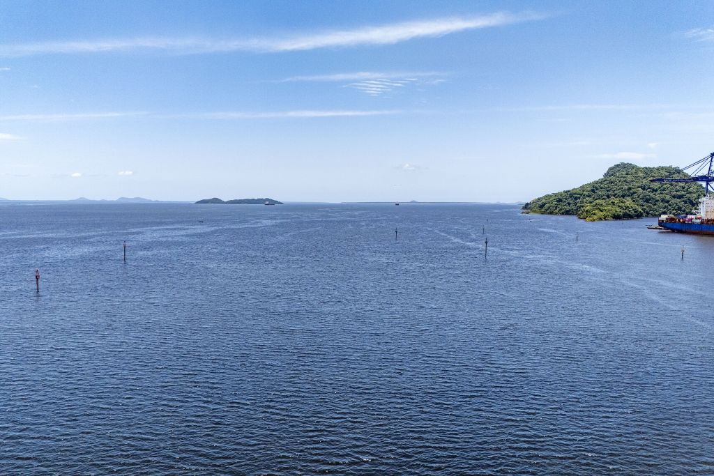 Vista panorâmica do mar com pequenas ilhas ao fundo, além de estrutura portuária à direita. Céu azul e água tranquila tornando a paisagem serena. Ilha do Mel vai ganhar nova sinalização náutica no acesso a Nova Brasília e Encantadas
