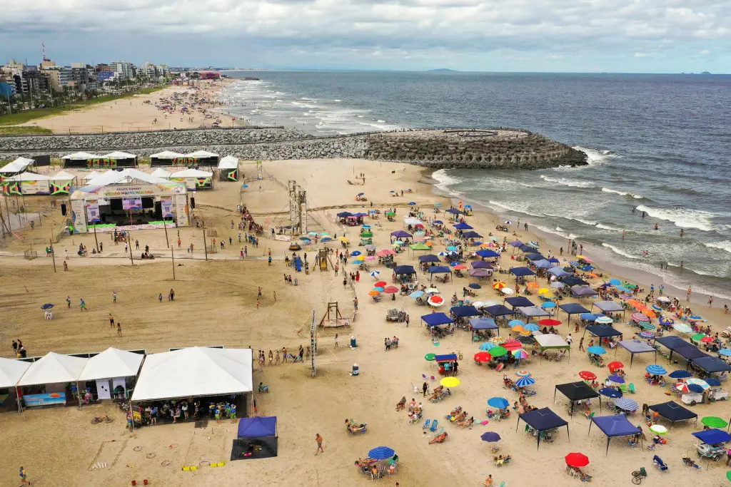 Vista aérea de uma praia movimentada com pessoas relaxando e se divertindo sob guarda-sóis coloridos, ideal para quem busca um dia de lazer à beira-mar. Sucesso de público, Verão Maior Paraná bate recordes e gera 1,4 mil novas empresas no litoral