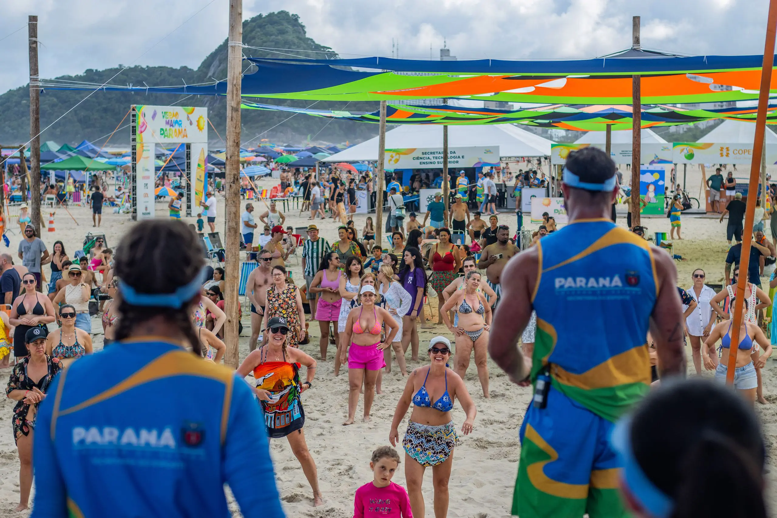 Gente se divertindo na praia com barracas coloridas ao fundo, mostrando um evento animado ao ar livre, cheio de tratamento acolhedor e atividades de lazer. Postos fixos do Verão Maior Paraná encerram atividades com 2,4 milhões de atendimentos