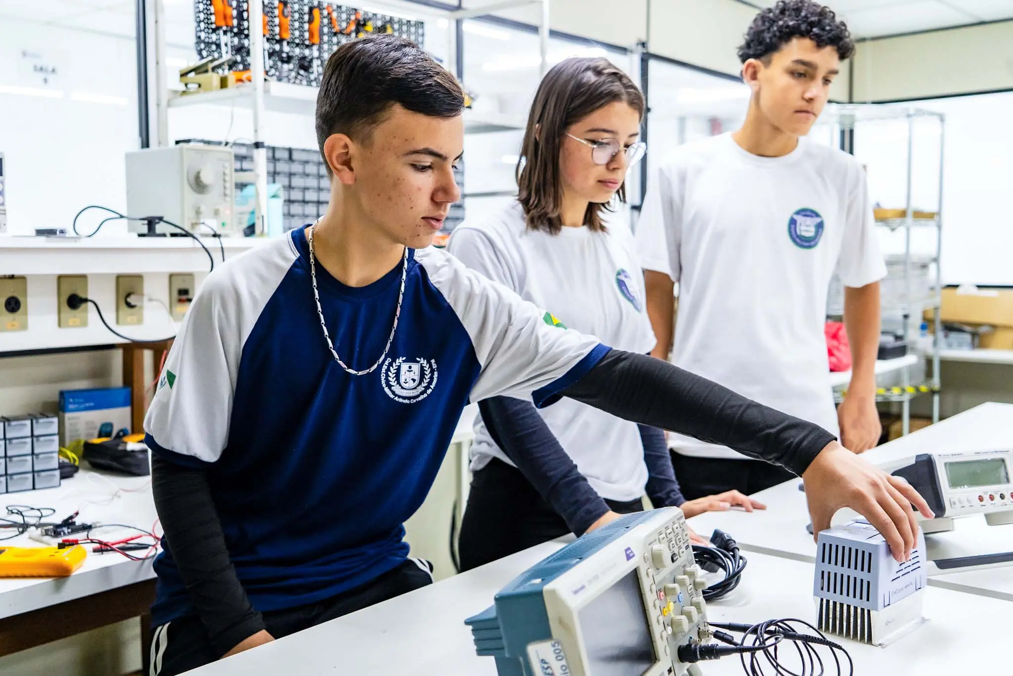 Estudantes em laboratório de eletrônica, manuseando equipamentos técnicos em atividade prática de aprendizado. A imagem destaca a importância da educação técnica.