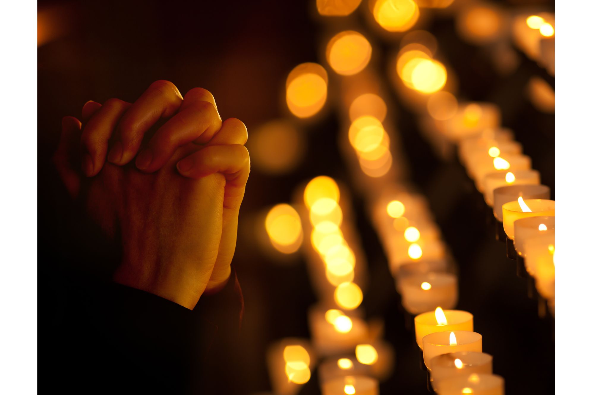 Imagem de mãos unidas em oração, cercadas por velas acesas, simbolizando reflexão e devoção em um ambiente sereno e espiritual. Carnaval: religiões explicam suas visões e posicionamentos sobre o período