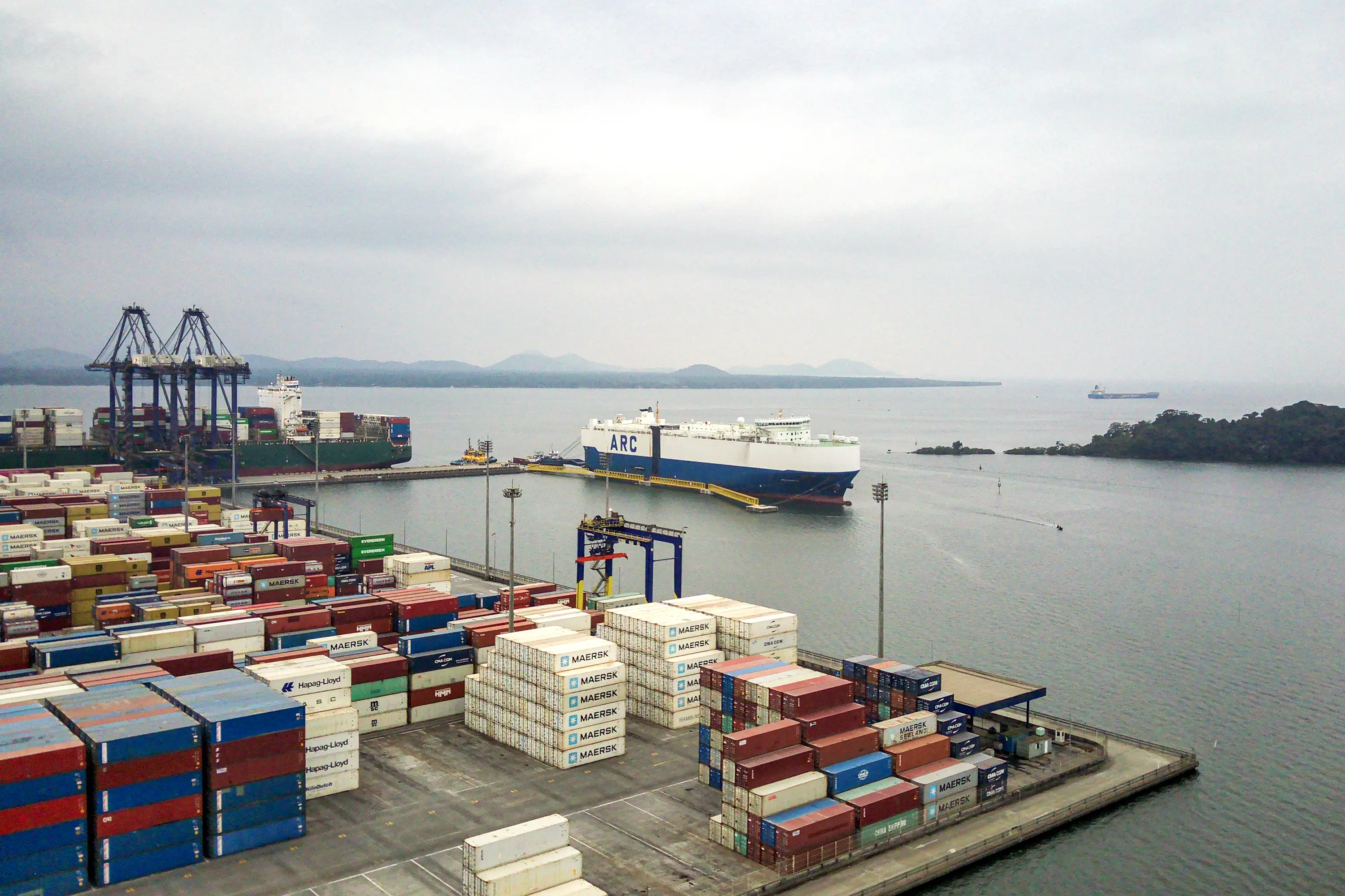 Vista panorâmica de um porto com contêineres coloridos armazenados, atraque de navios de carga e um ambiente aquático tranquilo. Novo calado do Porto de Paranaguá amplia capacidade de movimentação de contêineres