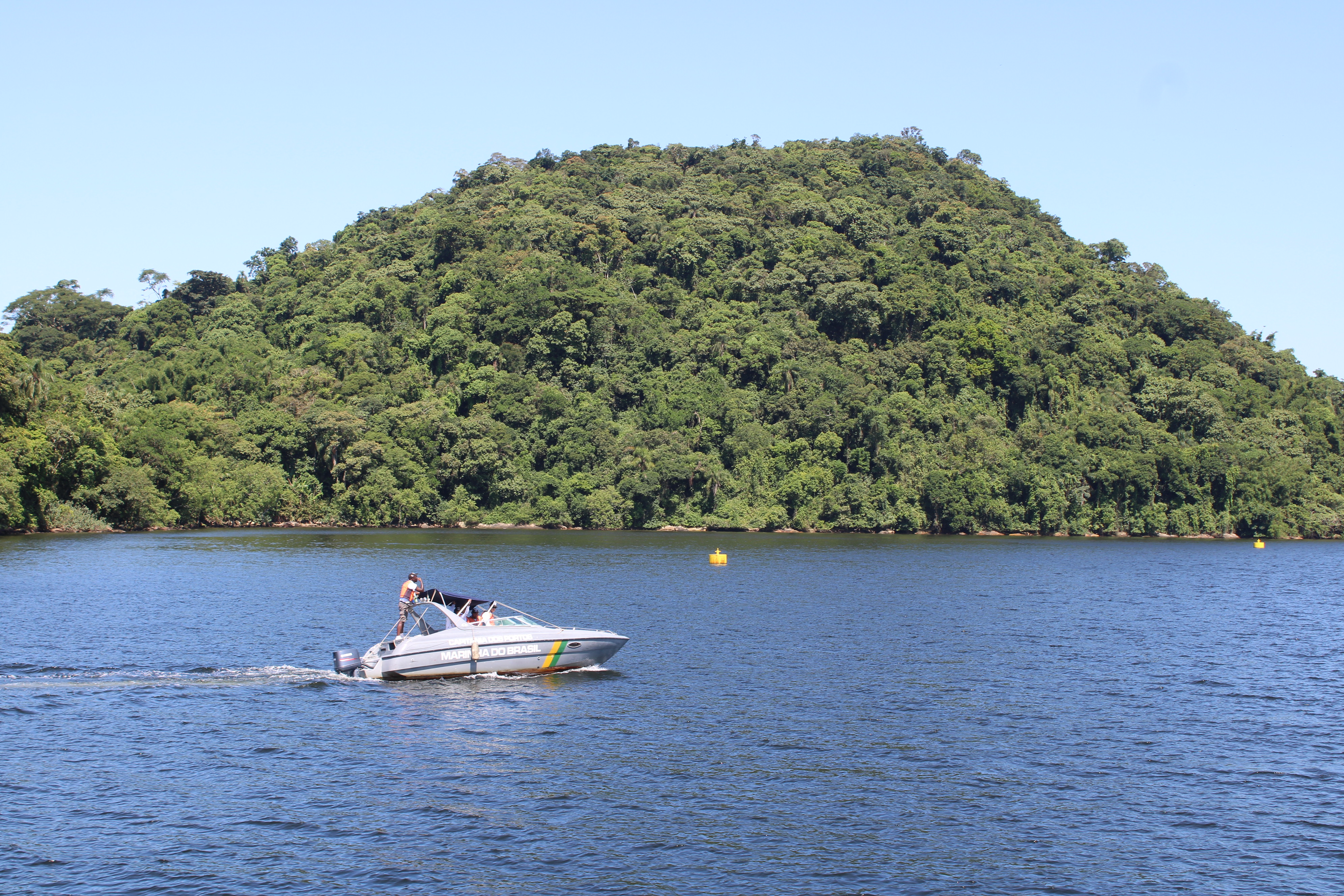 Um barco navega tranquilamente em um lago cercado por vegetação exuberante e montanhas. A cena evoca uma sensação de calma e natureza. Guardiã das águas: Marinha do Brasil e Portos do Paraná na fronteira da segurança e do desenvolvimento