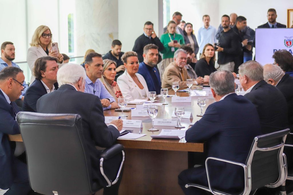 Novo marco regulatório da Ilha do Mel avança com instituição de comitê gestor 2 Reunião de líderes empresariais e políticos discutindo estratégias em um ambiente corporativo. Participantes estão ao redor de uma mesa com água e anotações. Novo marco regulatório da Ilha do Mel avança com instituição de comitê gestor